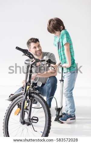 Happy father looking at son inflating bicycle tire with pump isolated on white