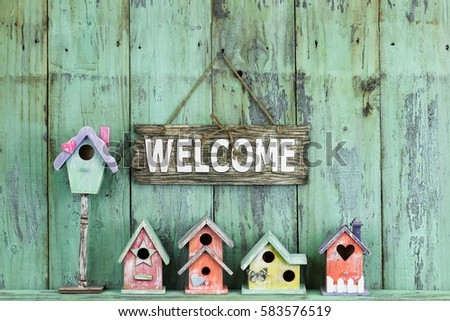 Welcome sign hanging over row of spring birdhouses by antique rustic mint green wood background; colorful springtime composition with wooden painted copy space