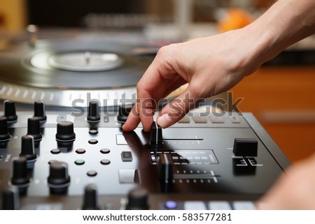Hip hop dj plays music with turntables. Disc jockey mixing vinyl records with musical tracks with professional sound mixer. Djs hand adjusting volume level on audio mixing controller device in studio