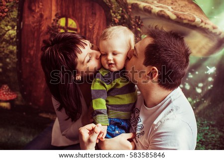 Mom and dad kiss their little son posing before fairy tail door painted on the wall