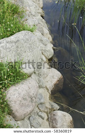 Stones between water with leaves on surface and green grass