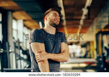 Handsome young man feeling the pain in hand at the gym Royalty-Free Stock Photo #583610284