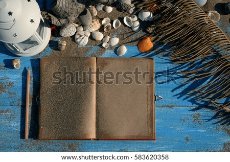 white wooden background with sand and shells, antique notebook and pencil
