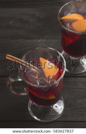 Two glasses of hot mulled wine with orange, star anise and cinnamon stick on wooden background. Steam rises over the glasses. Romantic and homely atmosphere, holiday mood