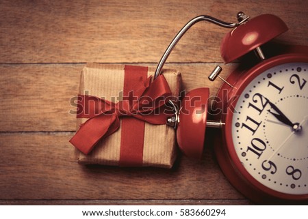beautiful gift and red alarm clock and lying on the wonderful brown wooden background