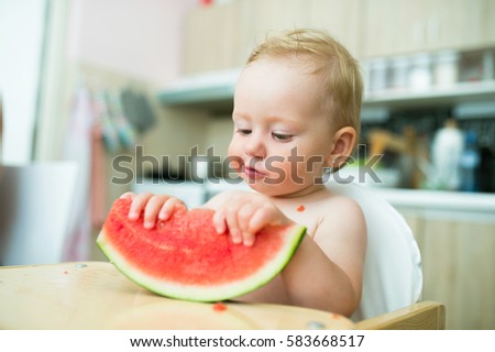 Cute little girl sitting in high chair eating watermelon