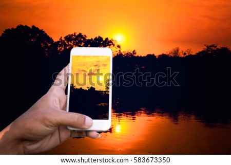 Person is taking photo sunset above the river with a smartphone.