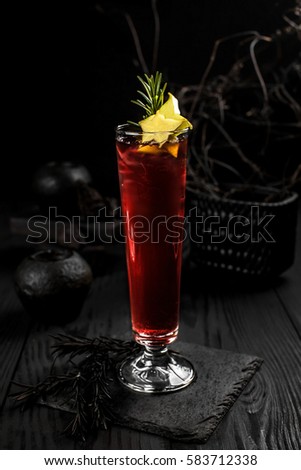 Cocktail red, decorated with slices of cannon and rosemary on a black wooden background with decor