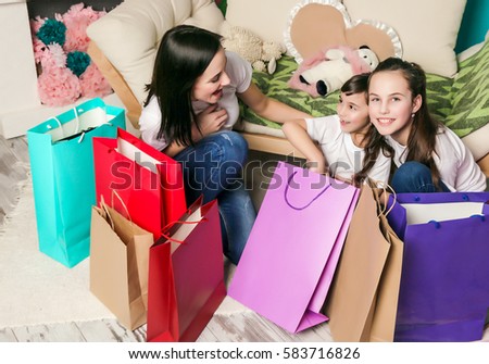 Emotions happiness mother and little cute daughter look in the colored bags near sofa after fun family shopping. 