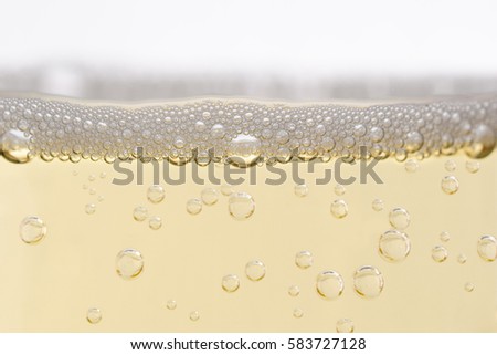 Close up (macro) of  champagne glass, filled with sparkling white wine.  Rising bubbles topped by layer of froth. Eye level shot. Royalty-Free Stock Photo #583727128