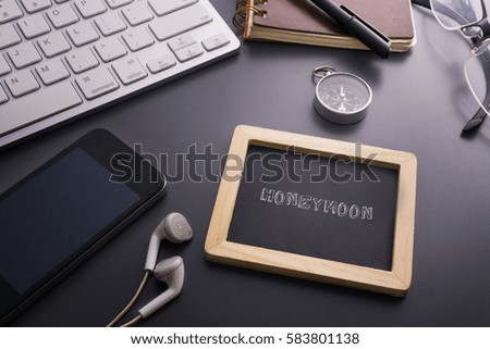 Vacation and travel concept.HONEYMOON written on small chalkboard and smart phone,earphone,compass,glasses,notebook,pen,keyboard on the grey background