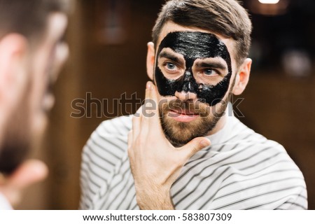 Young man with facial mask looking in mirror Royalty-Free Stock Photo #583807309
