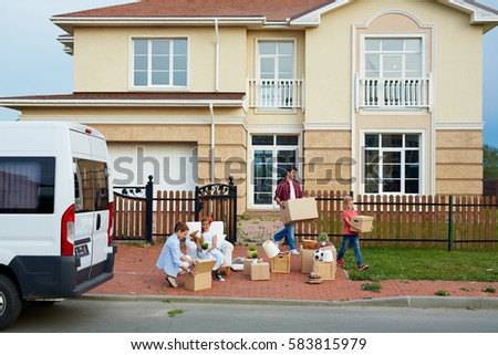 Portrait of family with two children moving out: mother and daughter busy sorting personal belongings in front of house while father and son taking out cardboard boxes to van outside Royalty-Free Stock Photo #583815979