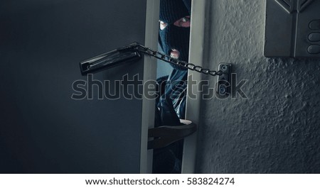 dangerous masked burglar with crowbar breaking into a victim's home door Royalty-Free Stock Photo #583824274