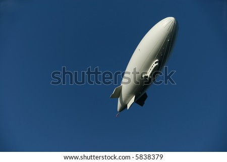 A large blimp in a cloudless deep blue sky.  It is side lit by the setting sun.  It is white and completely free of graphics.