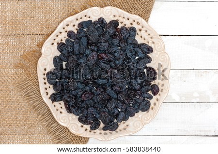 Raisins on a plate, white wooden background, top view, space for text.