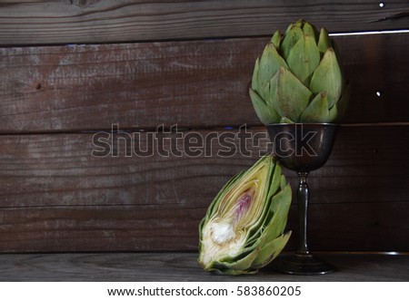A picture of a whole and a half of an artichoke with a wooden background.