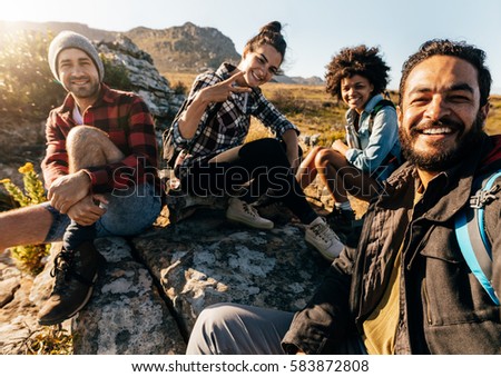 Group of friends resting on mountain while hiking. Hikers relaxing and taking selfie.