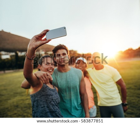 Group of runners taking selfie by smartphone at park. Young friends taking pictures outdoors after running session.
