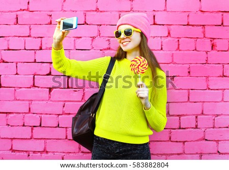 Fashion smiling girl taking photo selfie portrait using smartphone over colorful pink background