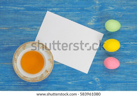 colorful eggs, tea cup and empty paper sheet on blue table
