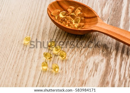 Vitamin D capsules in a wooden spoon on a wooden background, fish oil softgels, health and diet concept 