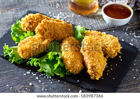 Spicy Fried Breaded chicken wings and a glass of beer on a wooden table. Royalty-Free Stock Photo #583987366