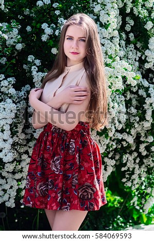 Portrait of a young girl in a cream blouse and red skirt spring bloom in the park opposite the bush