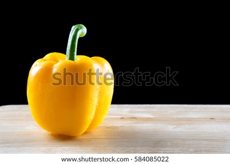 One yellow bell pepper on wood table, isolated on black