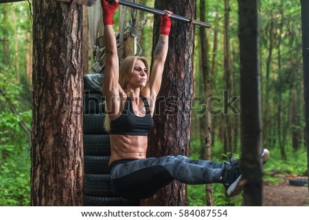 Fit woman doing hanging leg lifts abs muscles exercise on horisontal bar working out outside.