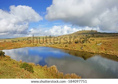Clouds and blue sky reflected in a small lake in winter time on Bodmin Moor, the Cheesewring can be seen in the distance, Cornwall, England, UK