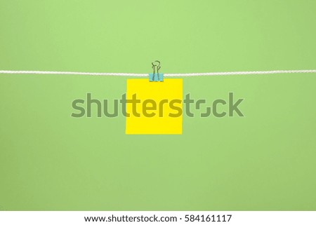 Blank yellow paper sheet on the string over green background