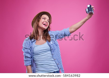 Mid shot of exhilarated woman smiling while making selfie photo. Wearing checked shirt and straw hat