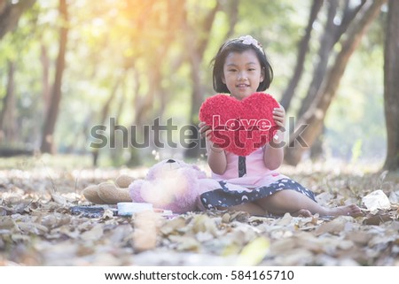 Little asian cute girl sitting on the ground  floor with her teddy bear holding a red heart-shaped pillow.Her smiling face and happy.