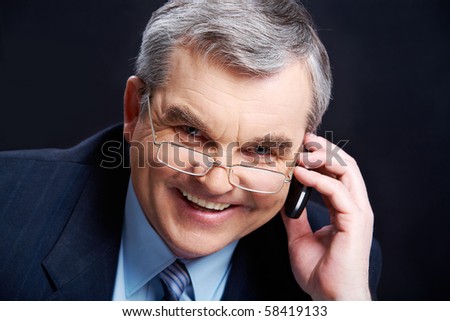 Photo of senior employer speaking by mobile phone on black background