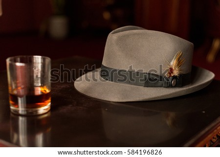 Glass of whiskey and men's hat on the wooden retro table