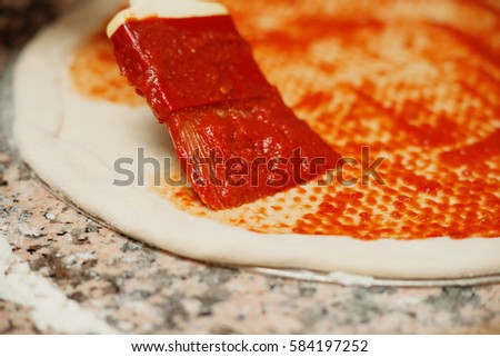 Spreading tomato sauce on a pizza 