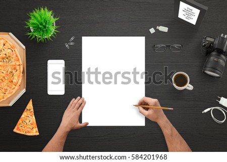 Designer or photographer sketching on empty white paper. Camera and mobile phone beside. Top view of black work desk.