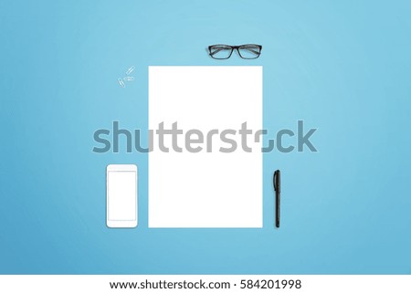 Clean paper with smart phone, glasses, pen and paper clips beside. Isolated screen for mockup. Blue desk in background.