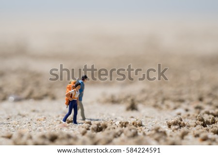 Travelling concepts. Two traveler miniature mini figures with backpack walking on sand beach under sunlight