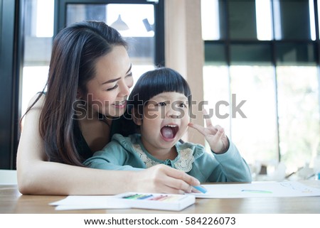 Pretty little girl with her mother painting picture at home. girl with her mom painting picture by 

colorful chalks at the table. Childhood and togetherness concept.