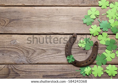 Background with rusty horseshoe and paper clover leaves on the old wooden boards. St.Patrick's day holiday symbol. Lucky charms.Space for text.