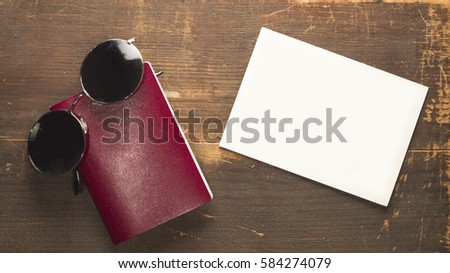 Blank red passport and round sunglasses with a blank post card on a wooden background