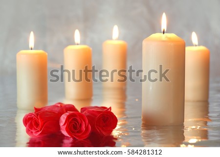 Group of burning candles with reflection and a group of red roses on the left