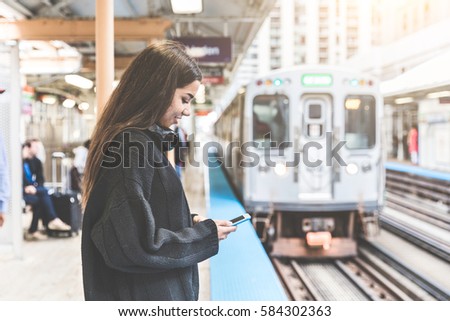 Girl with smart phone at train station in Chicago. Portrait of a young woman, mixed race, looking at the phone while waiting for the train on the platform Royalty-Free Stock Photo #584302363