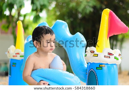 Asian kid playing in inflatable baby pool. Boy swim and splash in colorful swimming pool with water toys on hot summer day. shallow focus