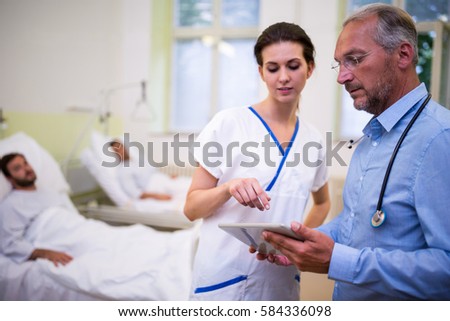 Close up of doctor and nurse discussing over digital tablet in ward at hospital