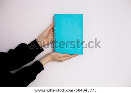 Hands holding a blue blank notebook or diary in a black jacket for any logo or design on a blank wall