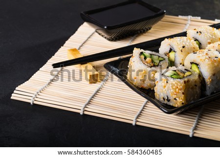 Uramaki sushi on black plate on bamboo napkin, black background