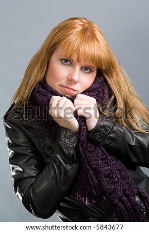 Attractive woman, huddling into her muffler with black leatherjacket. Gray background.